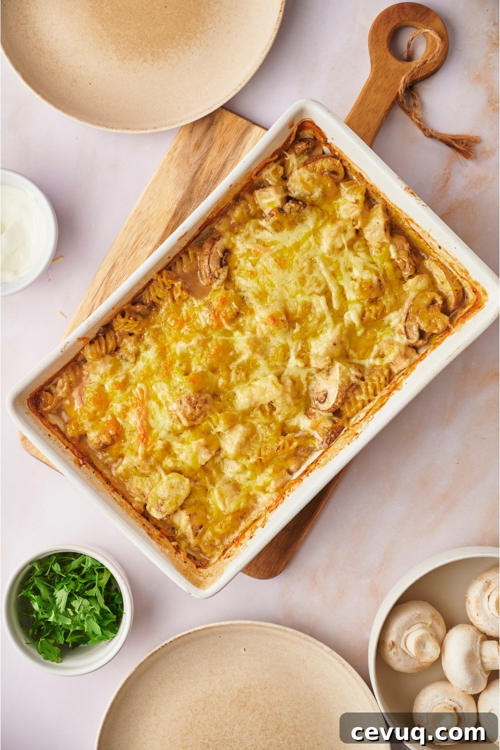 Chicken and mushroom casserole freshly baked in a white baking dish on a wooden board. Two empty plates surround the baking dish.