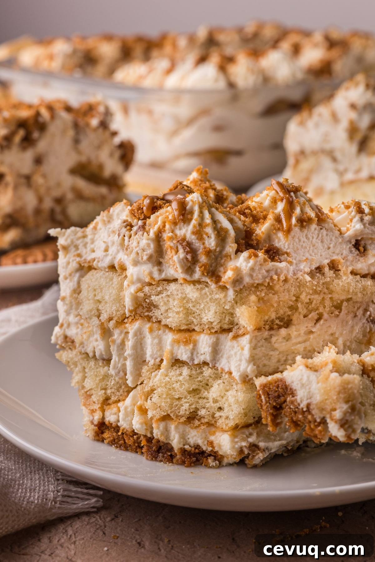 A close-up of a creamy layered Biscoff  tiramisu dessert on a plate with more in the background.