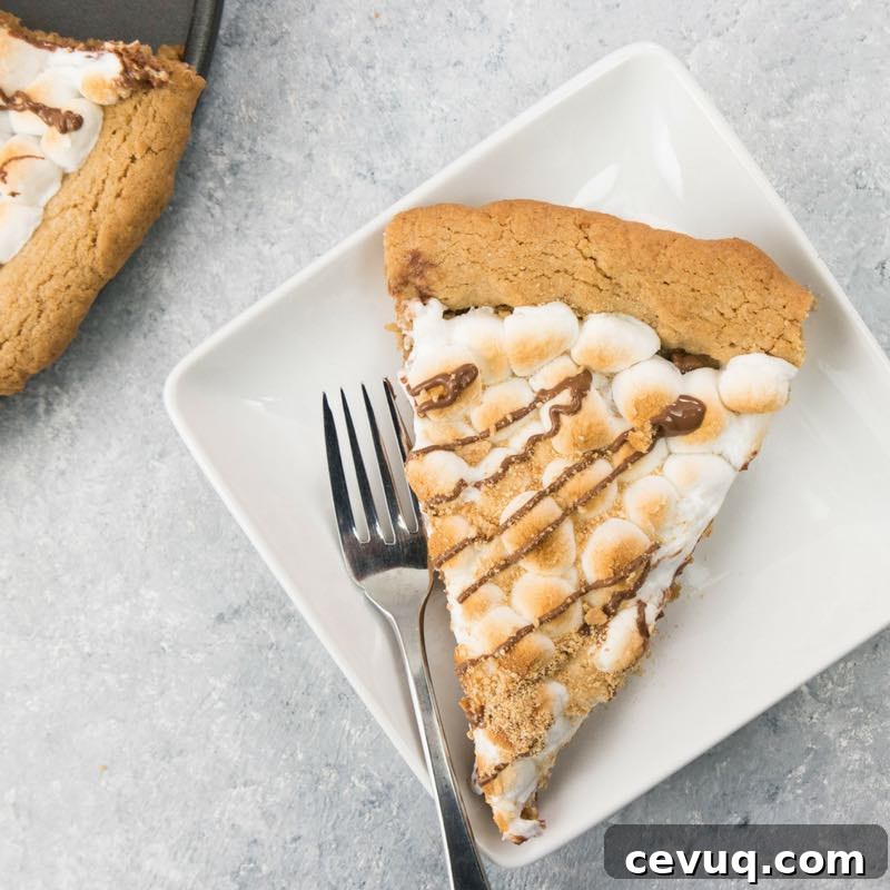 S'mores Dessert Pizza Recipe: Gooey Chocolate and Marshmallow Pie 4 This photo shows a piece of Smores Pizza served on a white dessert plate with a fork next to the pizza pan