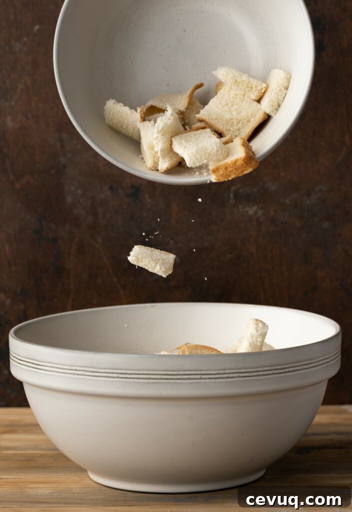 Adding cubed stale bread to a large mixing bowl to make bread pudding.