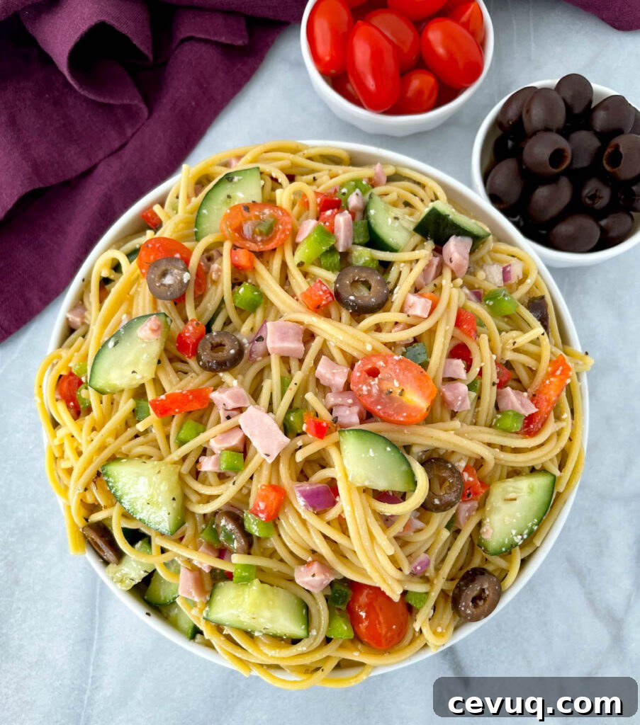 spaghetti salad in a white bowl with tomatoes and olivess