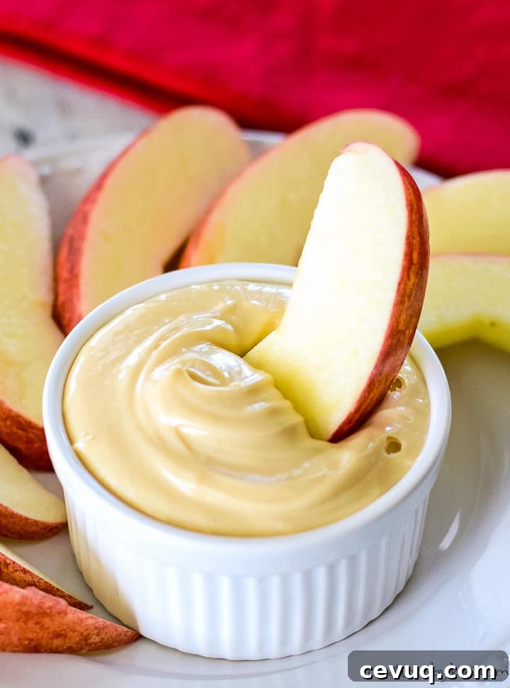 slice of apple being dipped in a bowl of caramel cream cheese apple dip