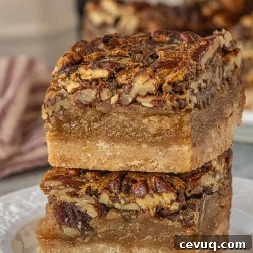 Close-up of two brown butter pecan pie bars stacked on a plate, showing the glossy pecan topping, thick gooey filling, and buttery shortbread crust with visible texture.