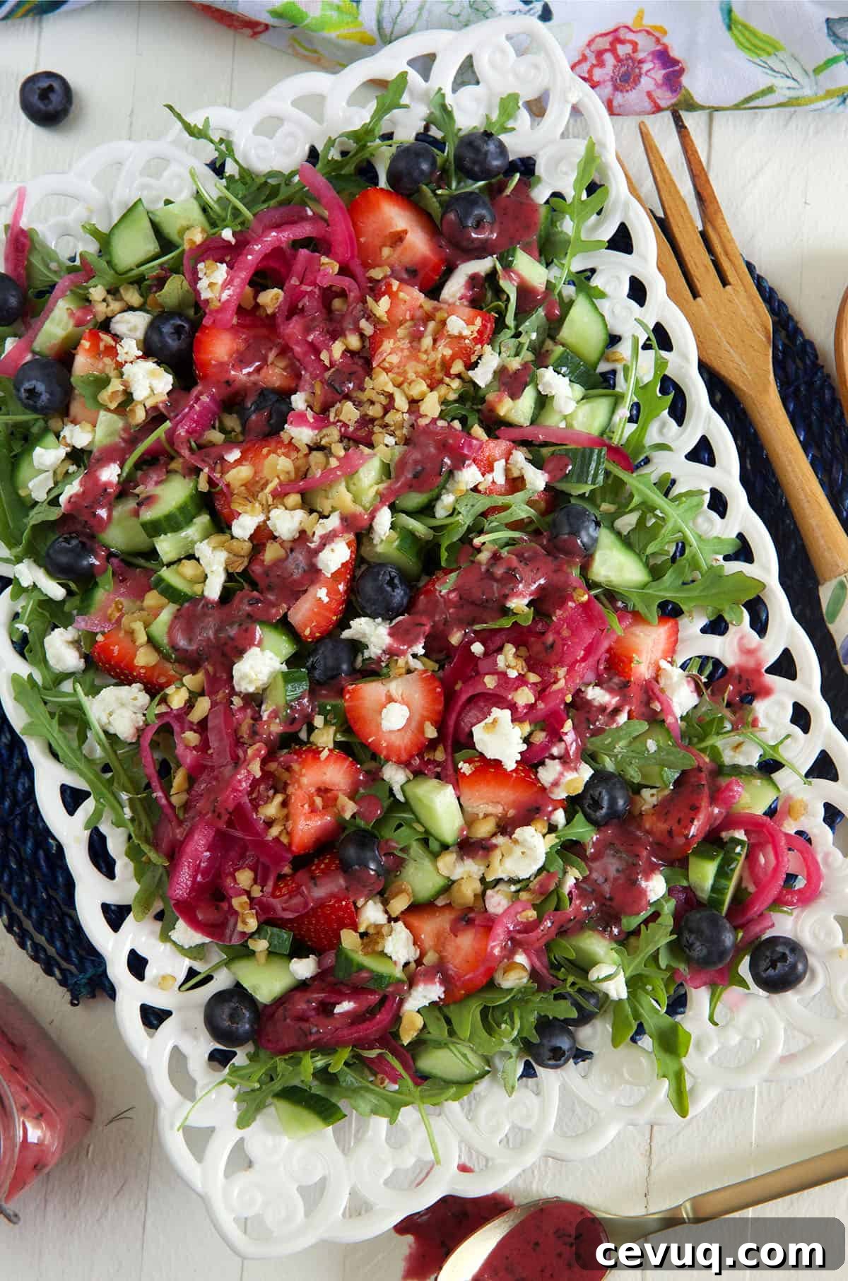 A white serving plate is topped with strawberry arugula salad.