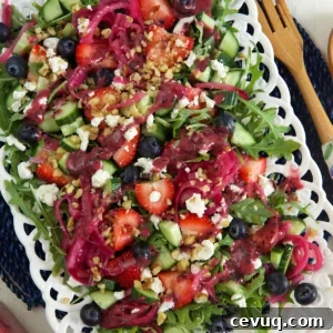 A white serving plate is topped with strawberry arugula salad.