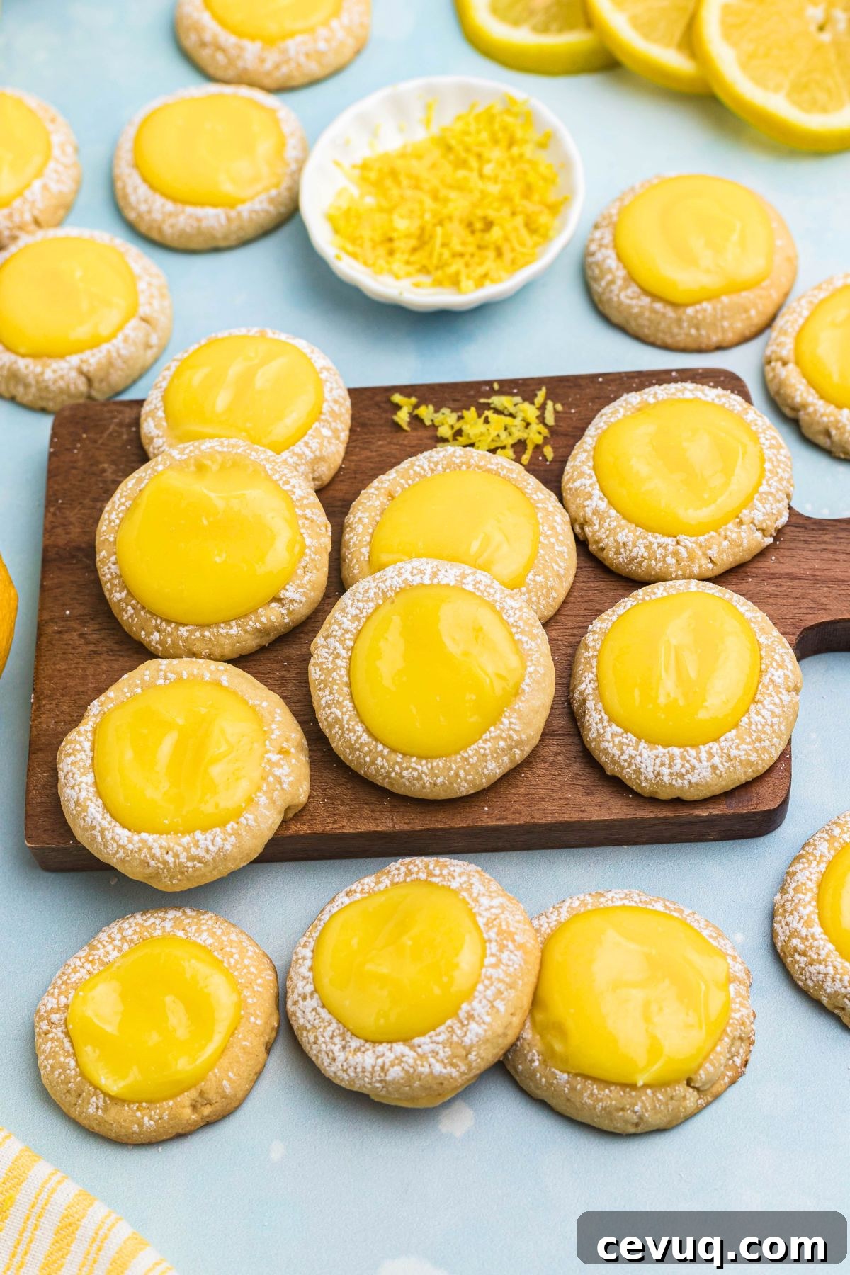 Lemon curd cookies on a small wooden board with lemon zest on the table in a small white bowl. 