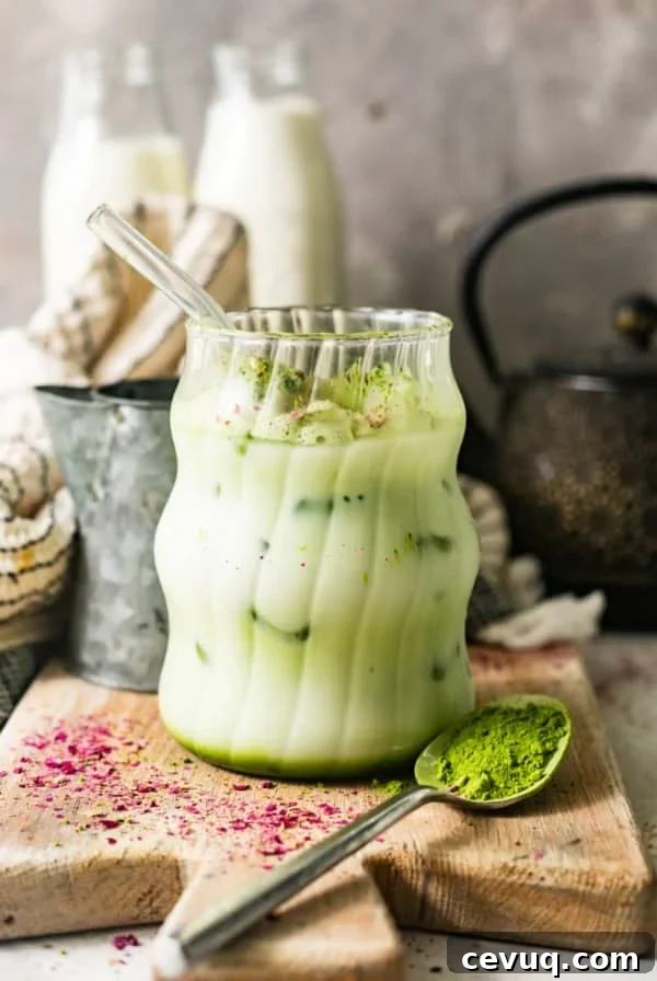 iced matcha latte in a cup with a straw on a serving board with small bottles of milk behind it.