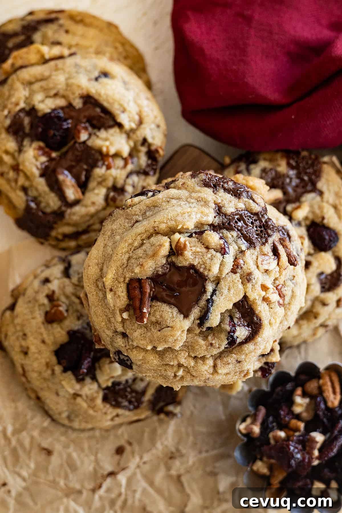 Dark Chocolate and Cranberry Cookies — Rich Chewy Recipe 6 Close up of top of cookie. Dark red napkin in the corner. A small cup of dried cranberries and pecans in another corner.