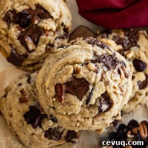Dark Chocolate and Cranberry Cookies — Rich Chewy Recipe 7 Close up of top of cookie. Dark red napkin in the corner. A small cup of dried cranberries and pecans in another corner.