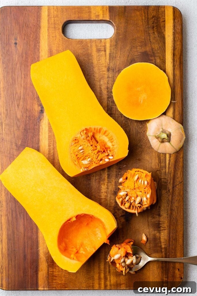 A peeled butternut squash cut in half with a spoon removing the pith and seeds.