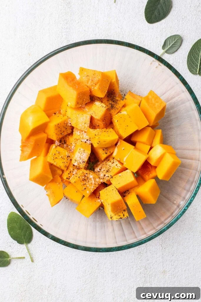 A bowl of raw butternut squash cut into cubes, seasoned with olive oil, salt and pepper.