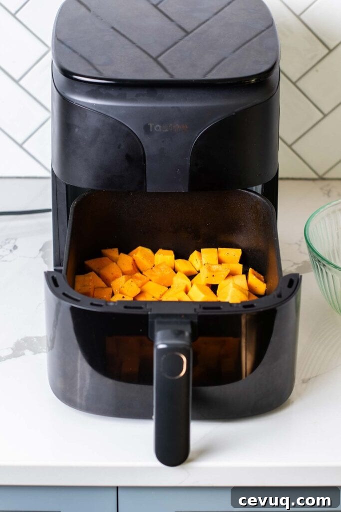 Butternut squash in an even layer in the air fryer basket.