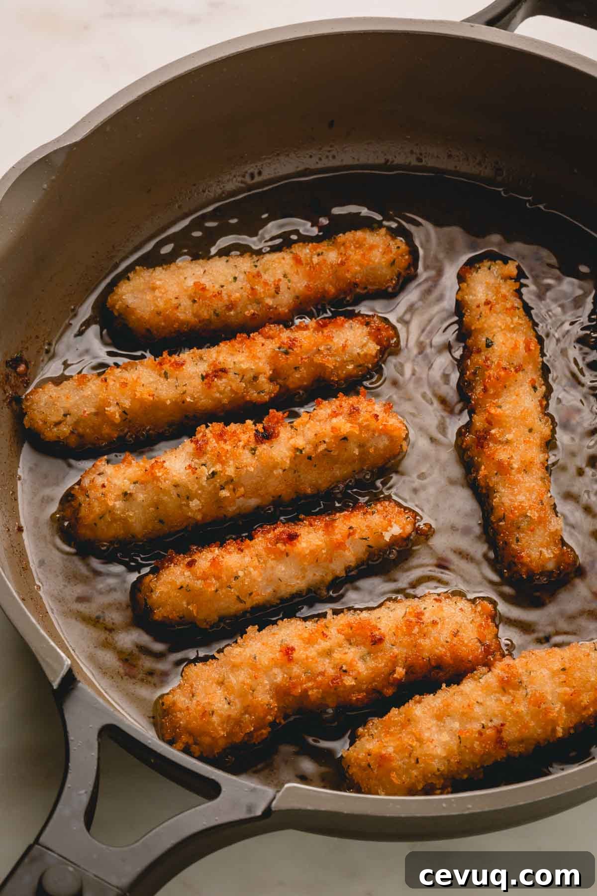Pork strips cooking in oil in a skillet.