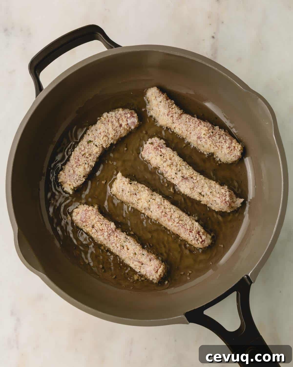 Breaded pork strips cooking in oil in a skillet.