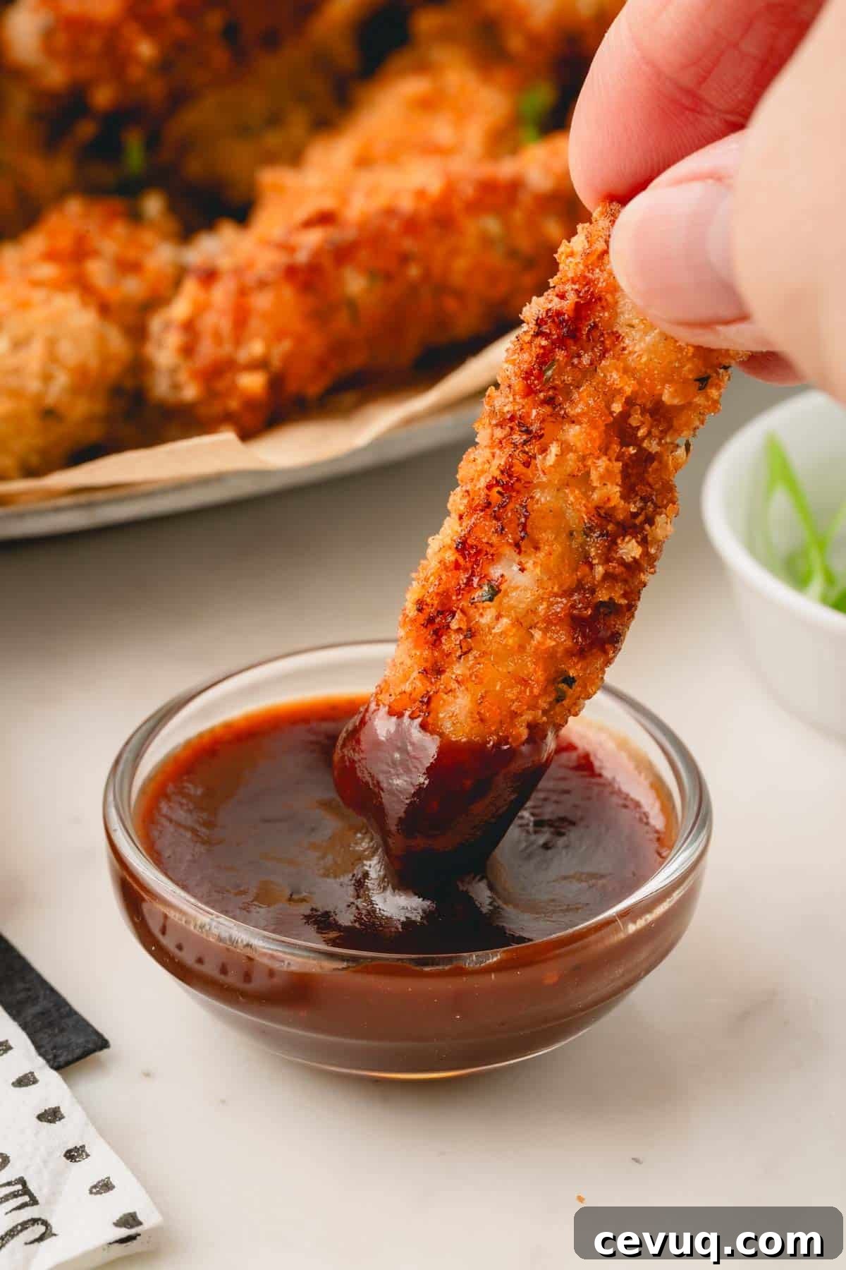 A pork strip being dipped in a bowl of BBQ sauce. 