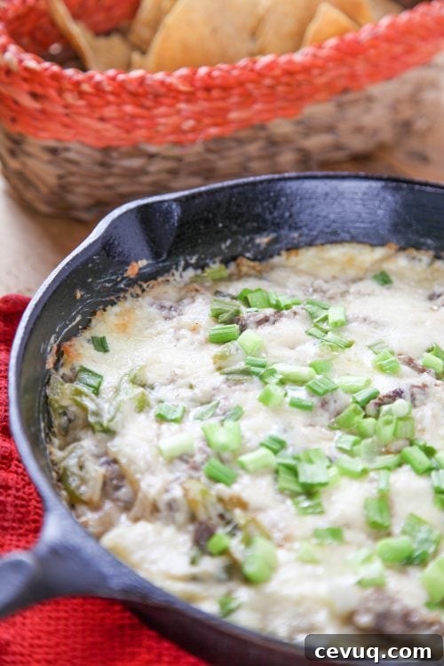 philly cheesesteak dip garnished with green onions in a cast iron skillet.