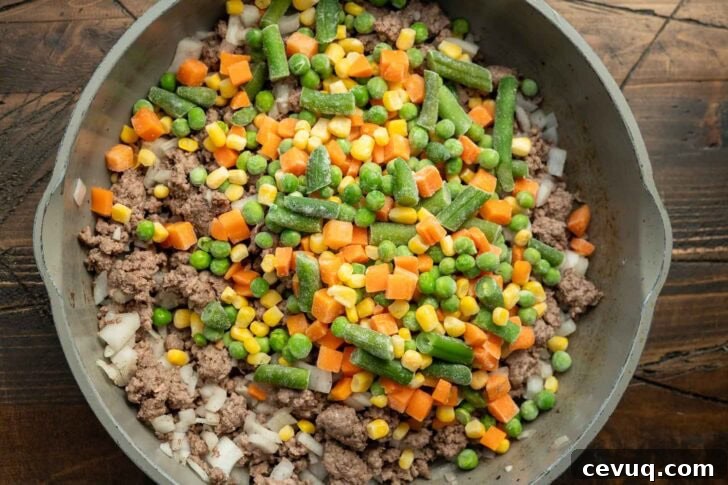 browned ground beef in a skillet with frozen mixed vegetables