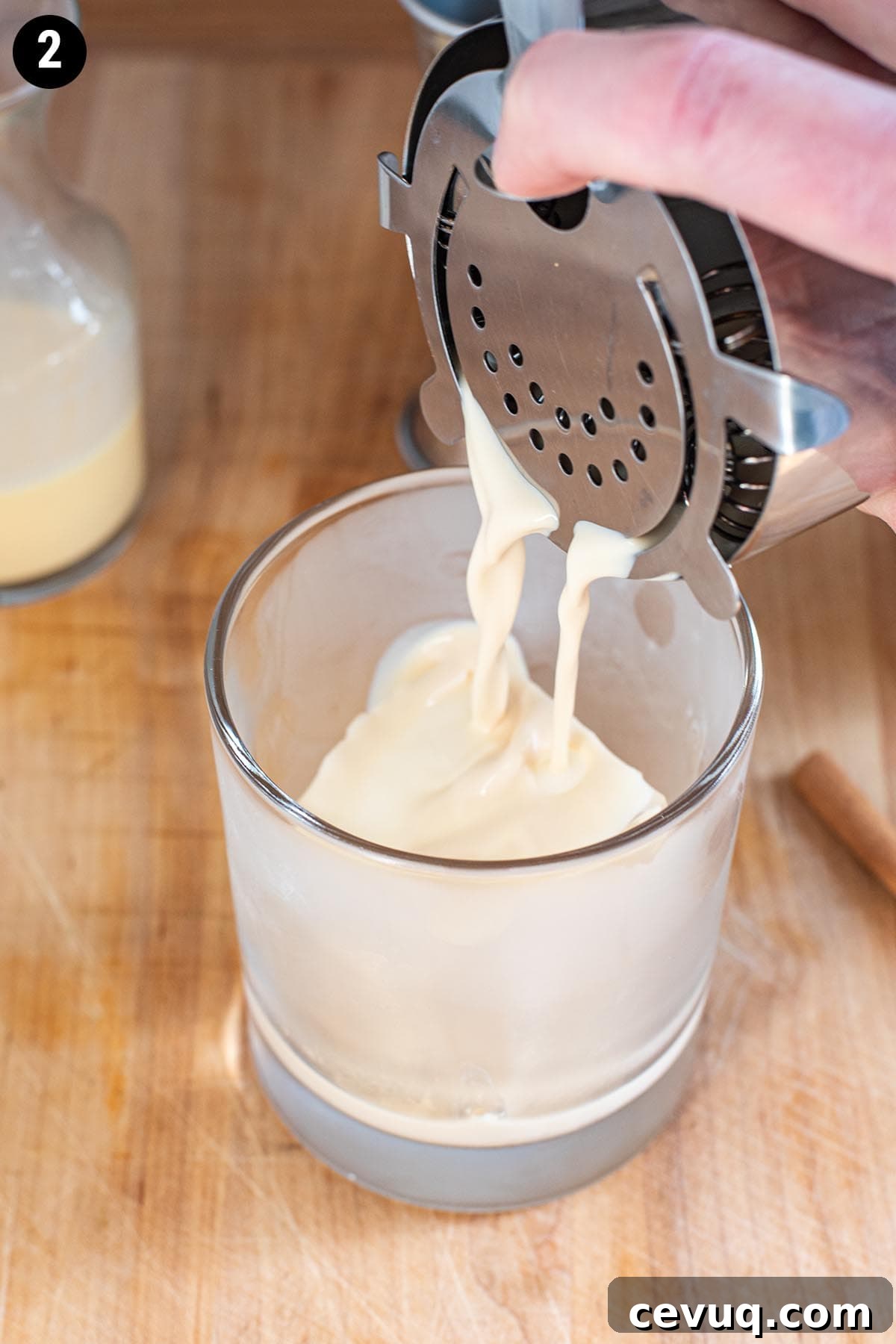 Straining an eggnog cocktail into a chilled double old fashioned glass with a large ice cube.
