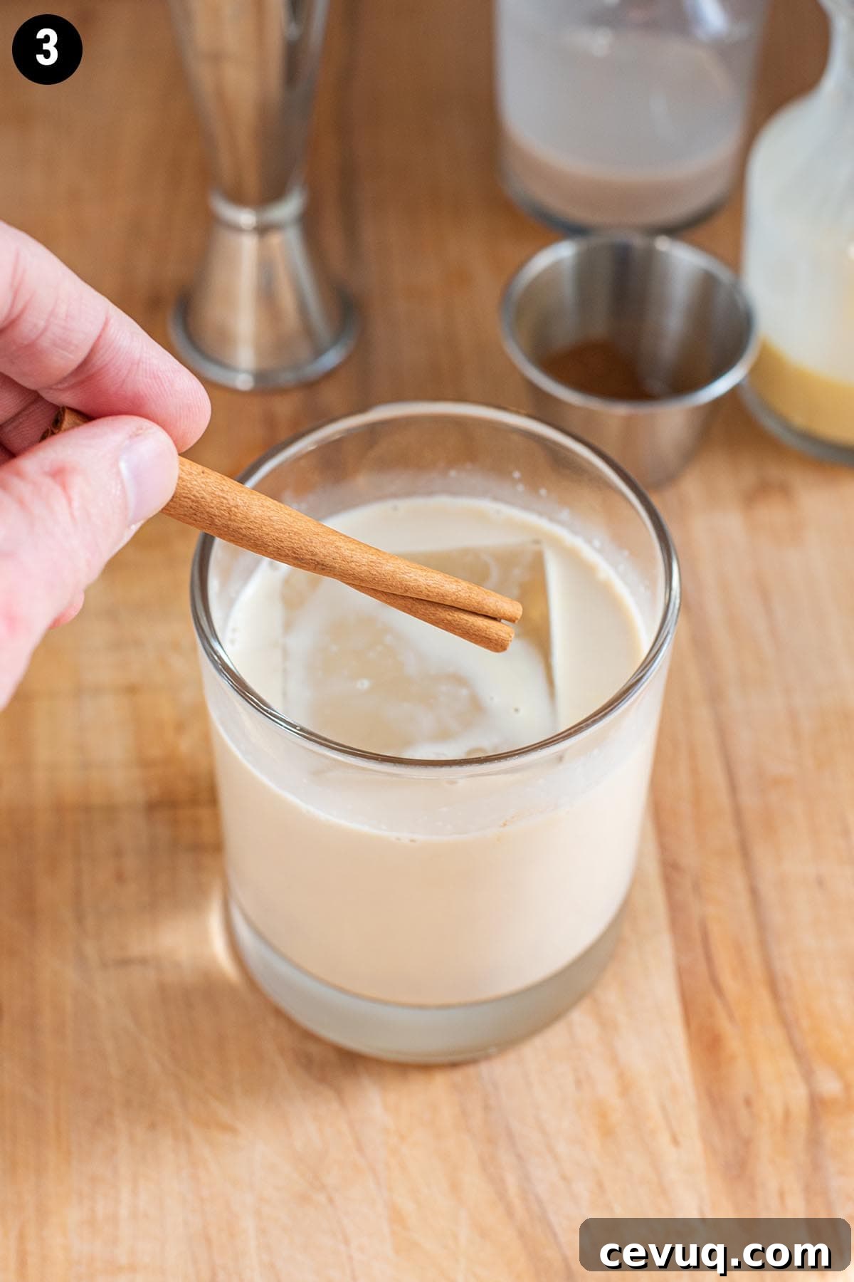 Adding a cinnamon stick garnish to an eggnog cocktail.