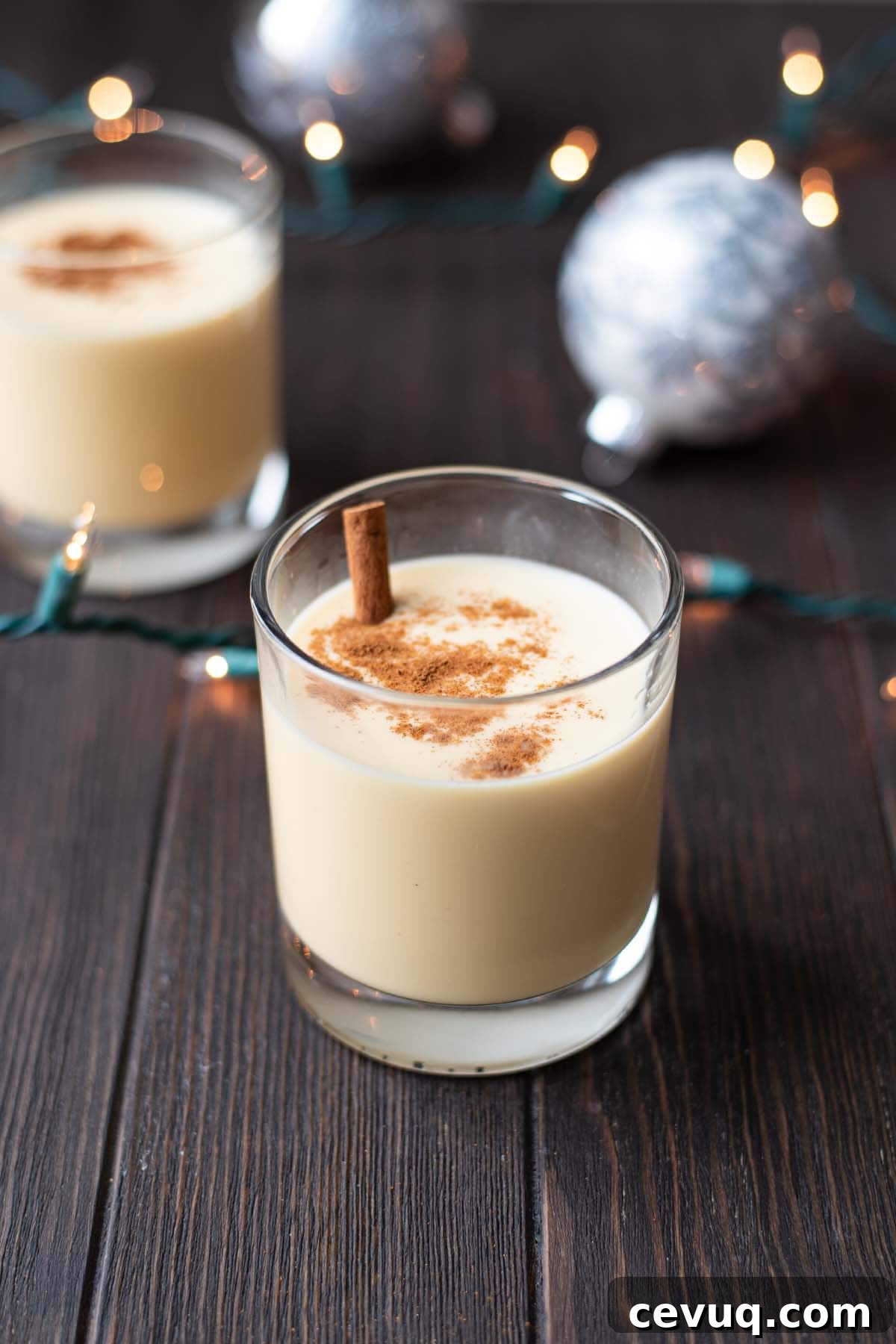 An eggnog cocktail on a dark wooden table with Christmas ornaments and Christmas lights.