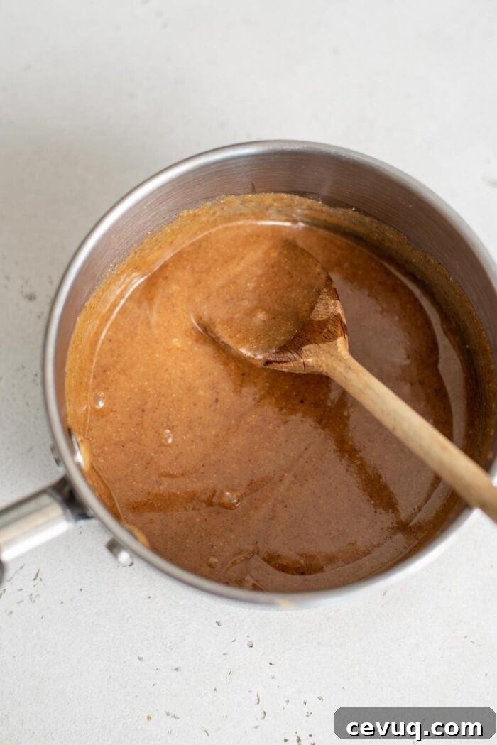 Almond butter and maple syrup mixed together in a small saucepan with a wooden spoon.