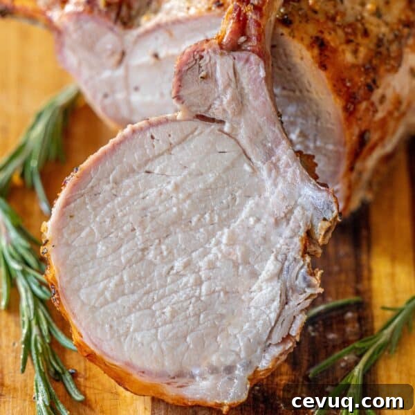 A roasted rack of pork, sliced to reveal its juicy interior, is displayed on a wooden board with fresh rosemary sprigs—a true showcase of the best roasted pork.