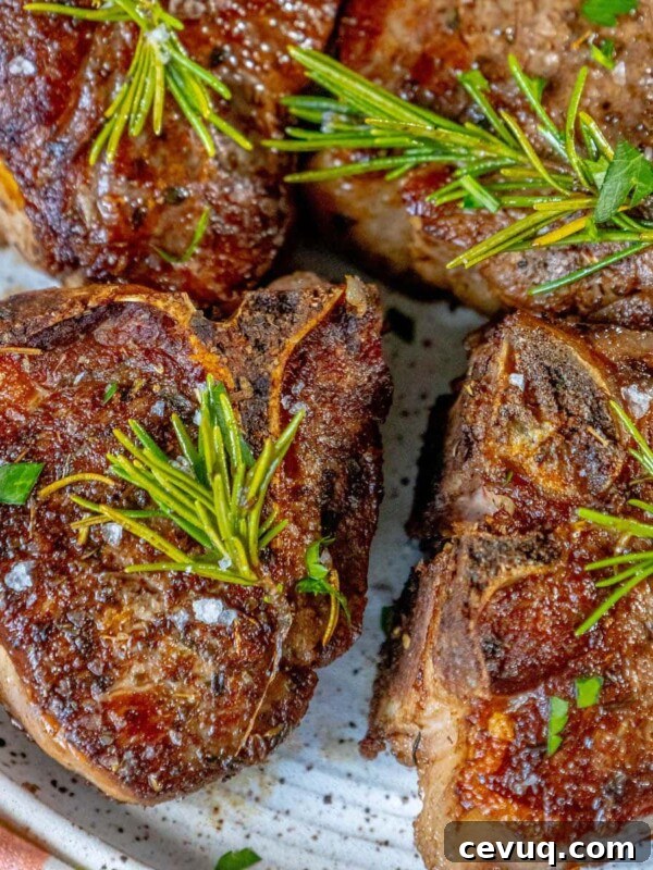 seared lamb chop on a white plate with a sprig of rosemary and sea salt flakes and a white wine shallot sauce on top