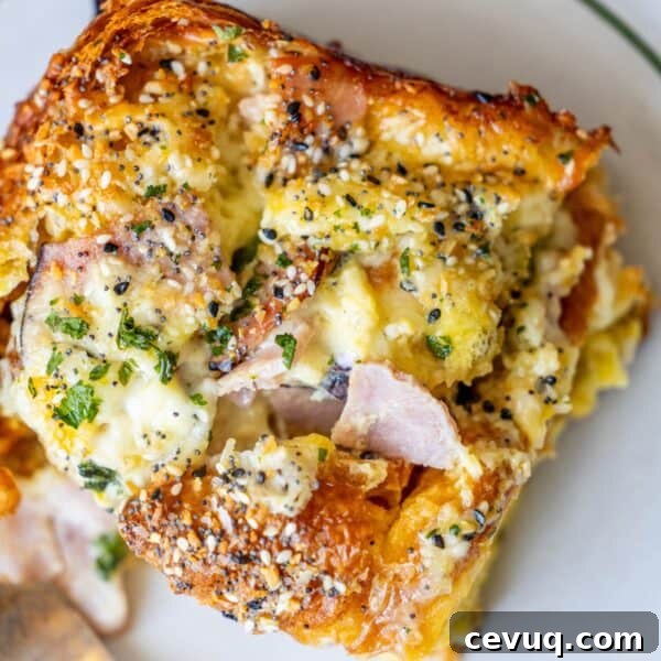 Close-up of a savory dish featuring ham, melted cheese, and an Everything Bagel seasoning blend on a croissant strata.