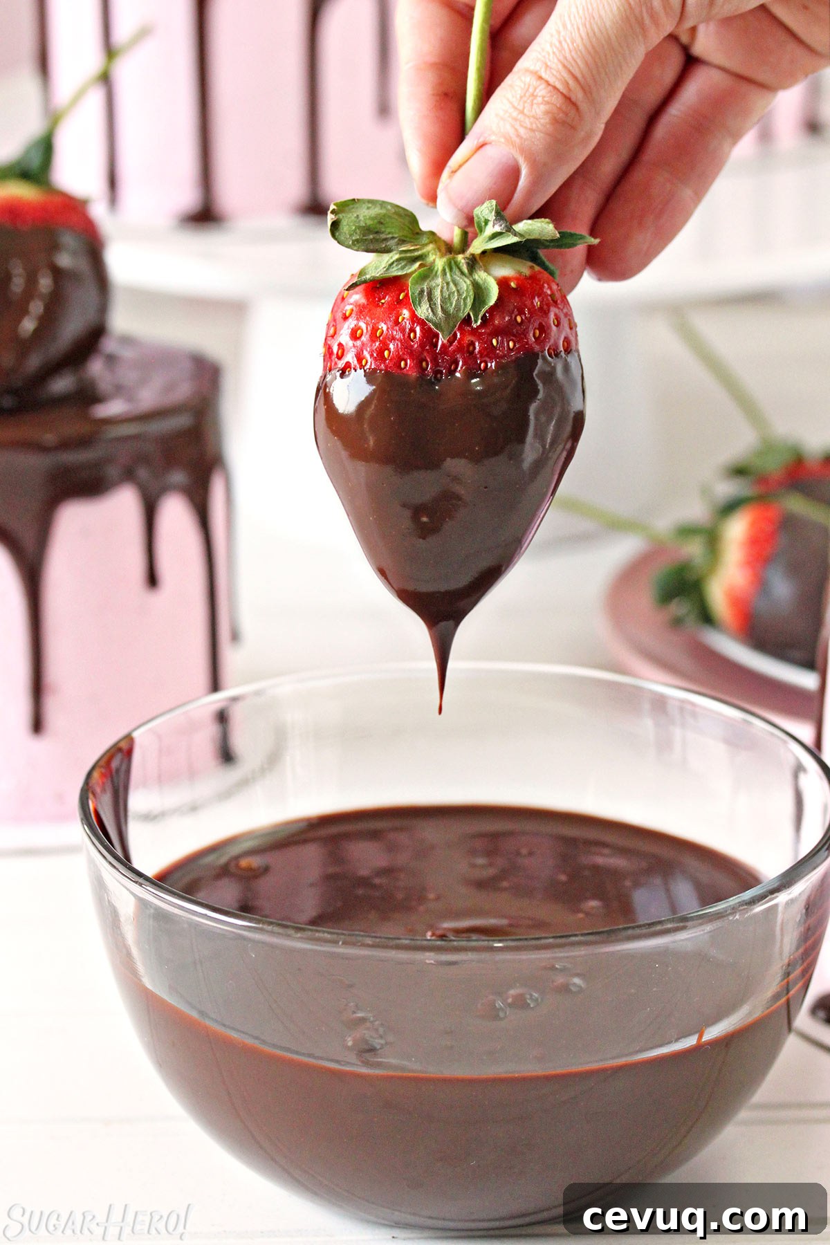 Chocolate-Covered Strawberry Mini Cake Recipe for Parties 4 Hand holding a large strawberry by the stem, dripping melted chocolate back into a chocolate bowl below.