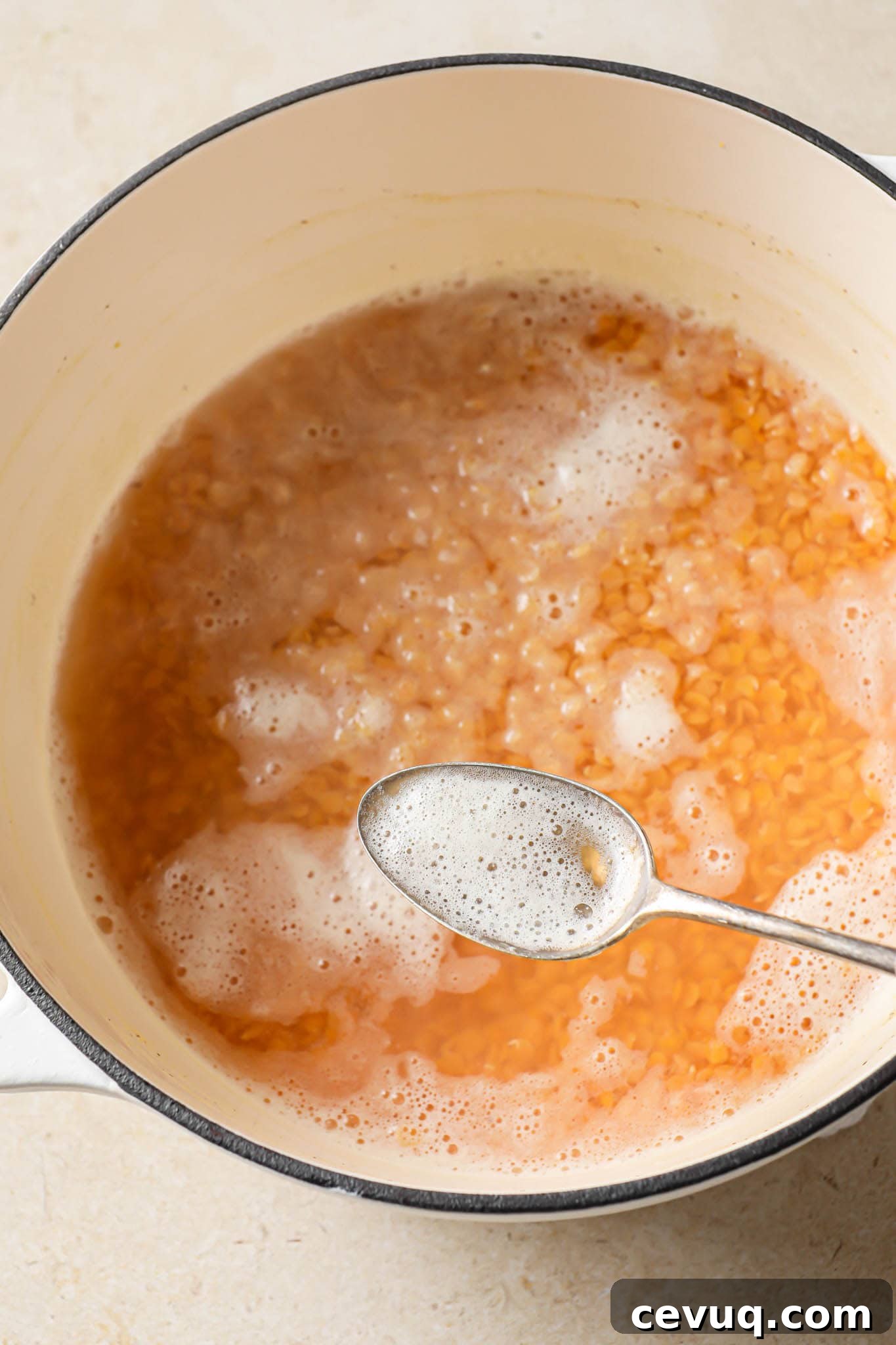 Removing scum from cooking red lentils.