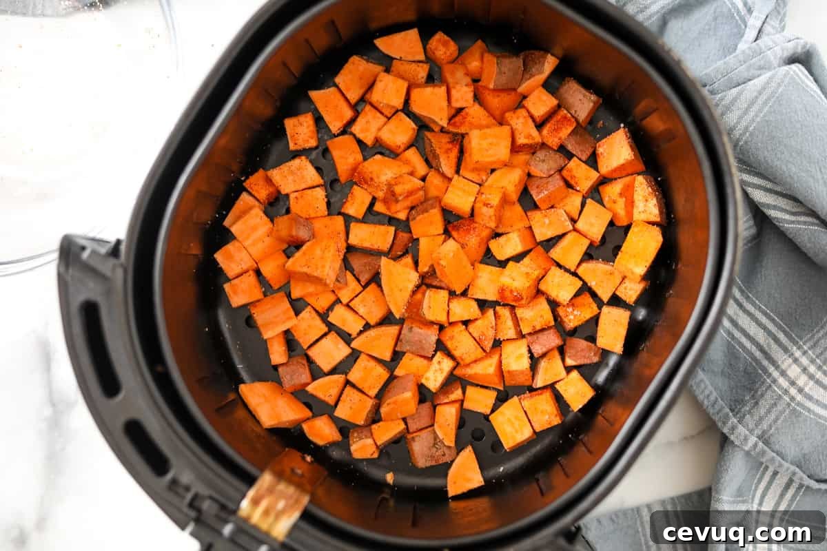 Air fryer basket with seasoned potatoes spread out in bottom of pan. 