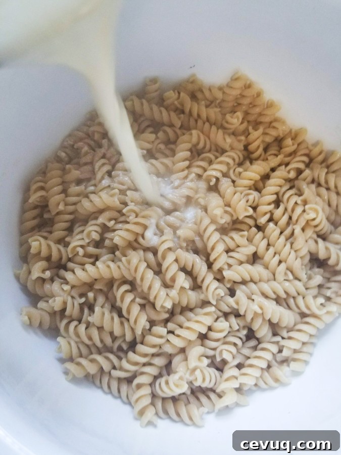 pouring alfredo sauce over pasta