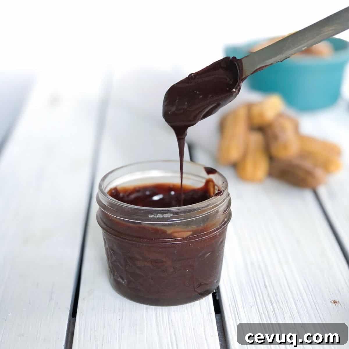 melted chocolate sauce in a small mason jar dripping off spoon.