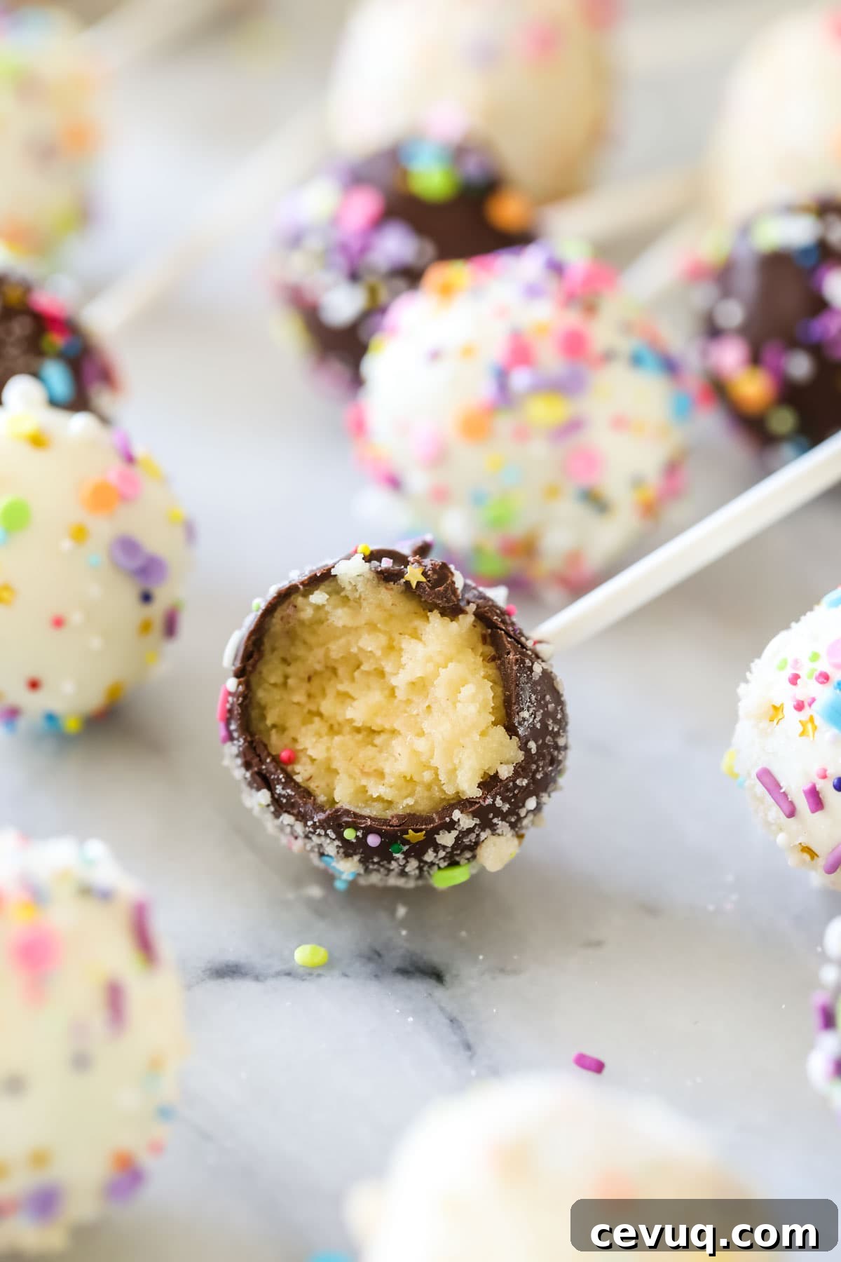 Chocolate covered cake pop bitten to show a yellow cake filling surrounded by other cake pops.