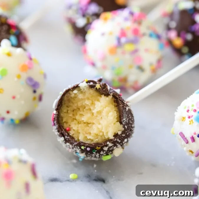 Chocolate covered cake pop bitten to show a yellow cake filling surrounded by other cake pops.