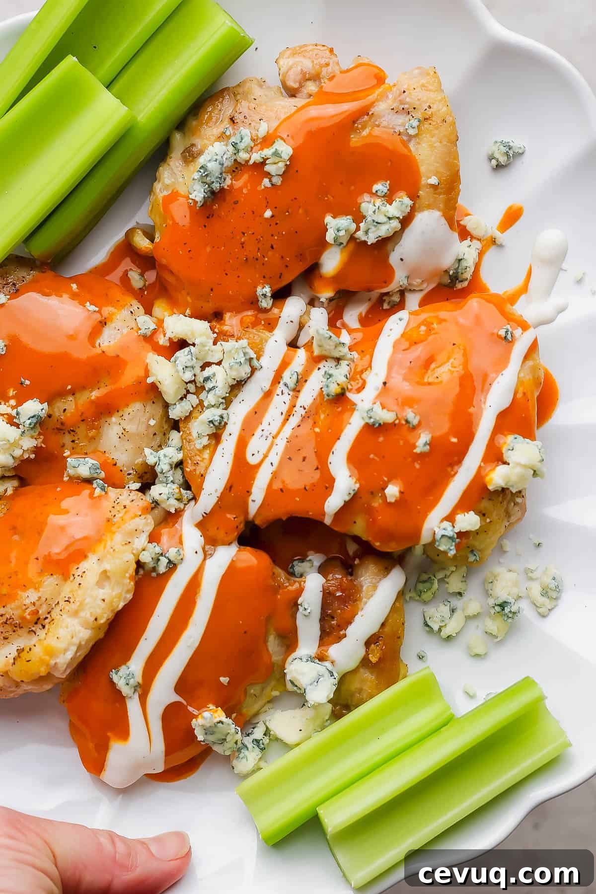 Buffalo chicken thighs on a plate topped with buffalo sauce and blue cheese garnished with celery.