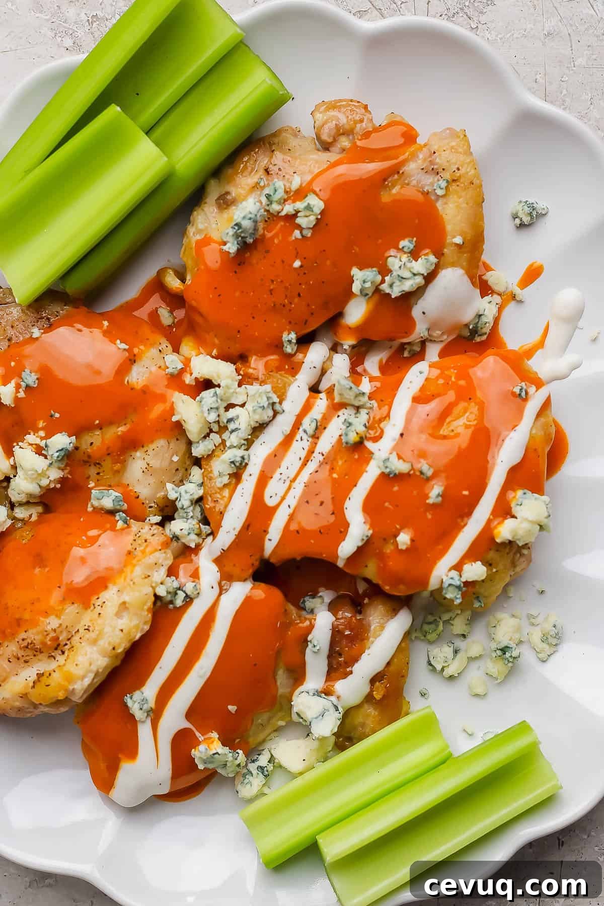 Chicken thighs on a plate topped with buffalo sauce, ranch dressing, and blue cheese.