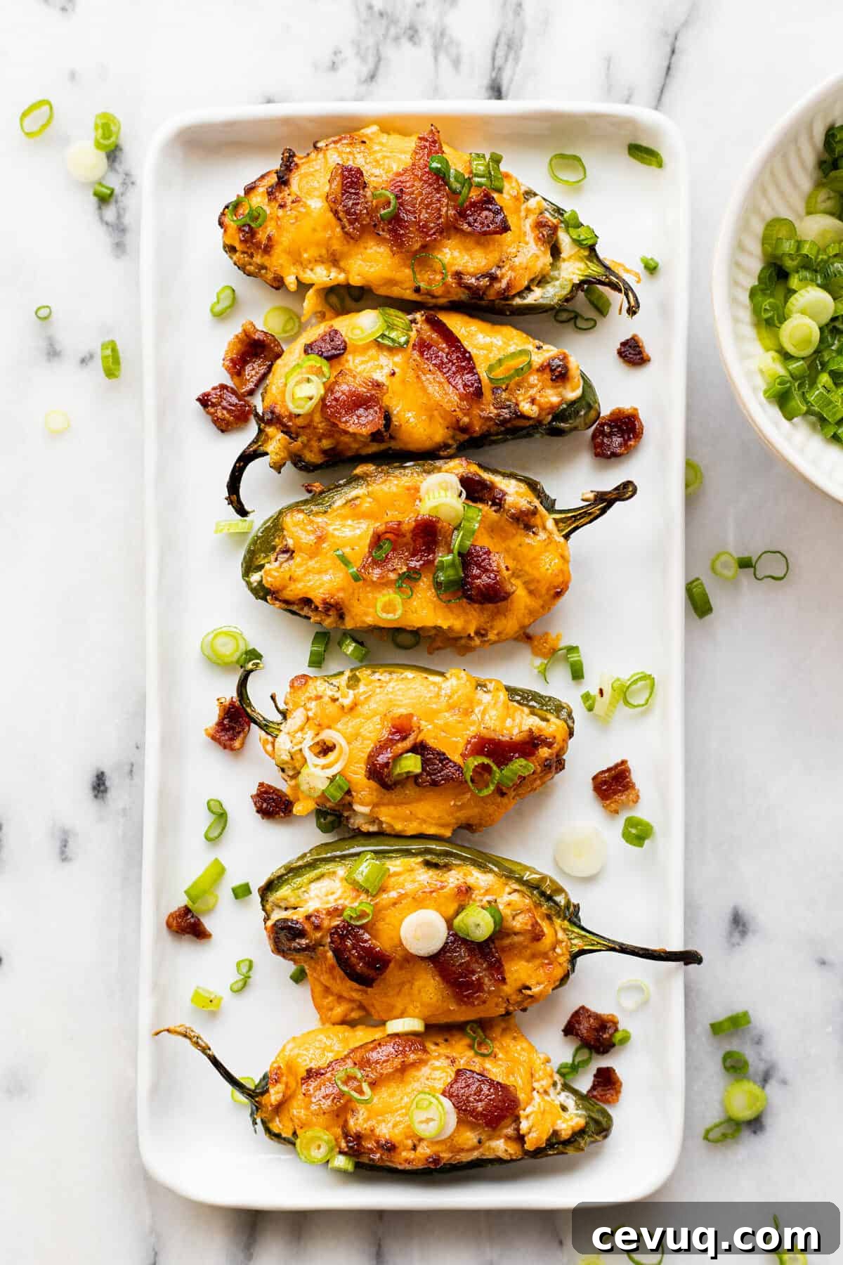 White plate filled with homemade air fryer jalapeno poppers garnished with sliced green onion.