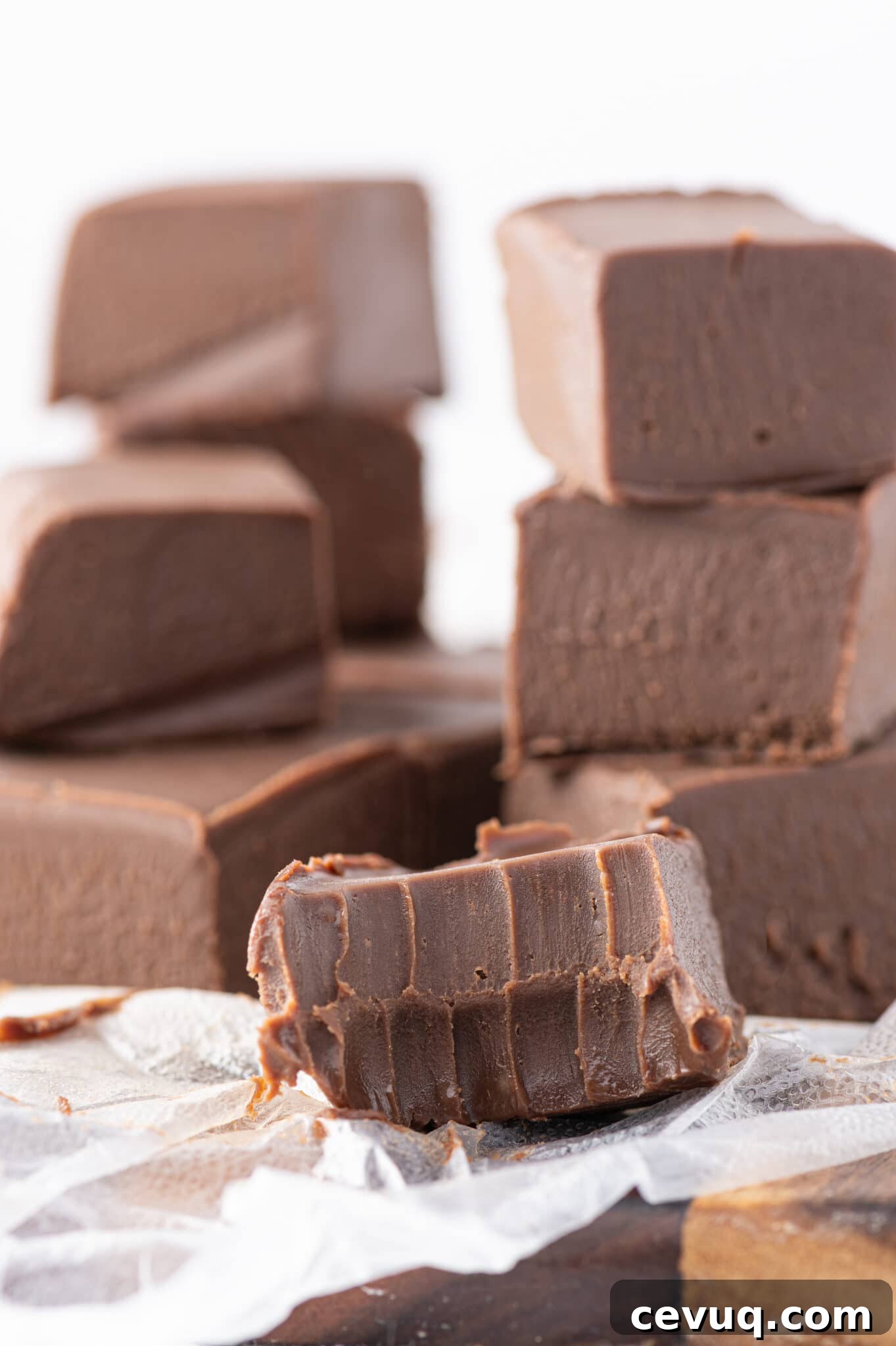 A piece of keto fudge in the foreground with a bite taken from it, with more fudge cubes from this recipe stacked in the background.
