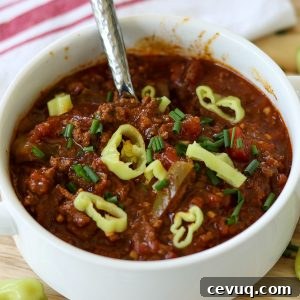 Square image closeup of finished chili served in a white bowl and garnished with pepperoncini.