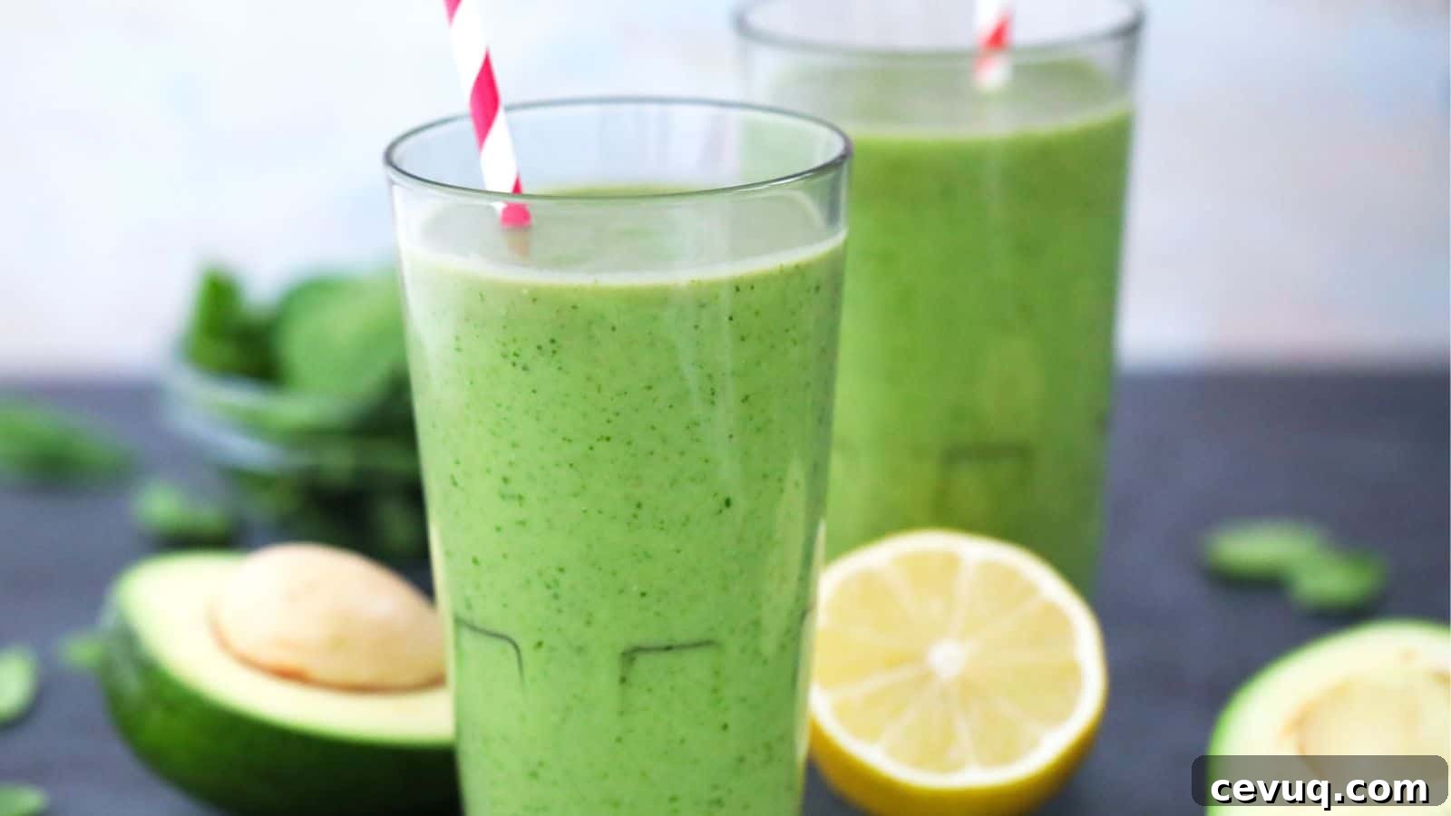 Two glasses of green smoothie with a lemon half and avocado in the background.