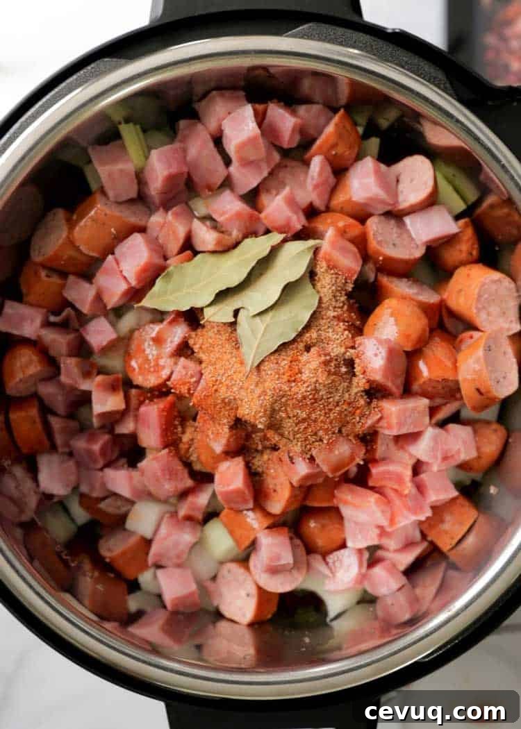 overhead: cubes of ham, andouille sausage and white onion with bay leaves and creole spices in pressure cooker