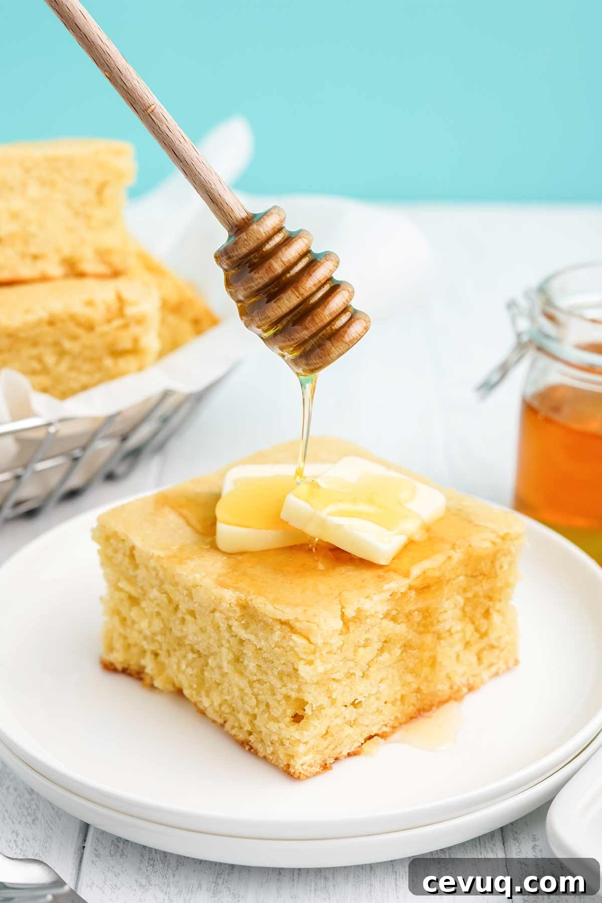 Square of cornbread with honey on a white plate with honey drizzling on top.