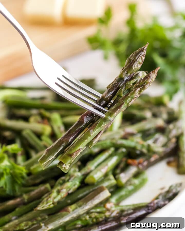 fork holding bites of asparagus from a white plate