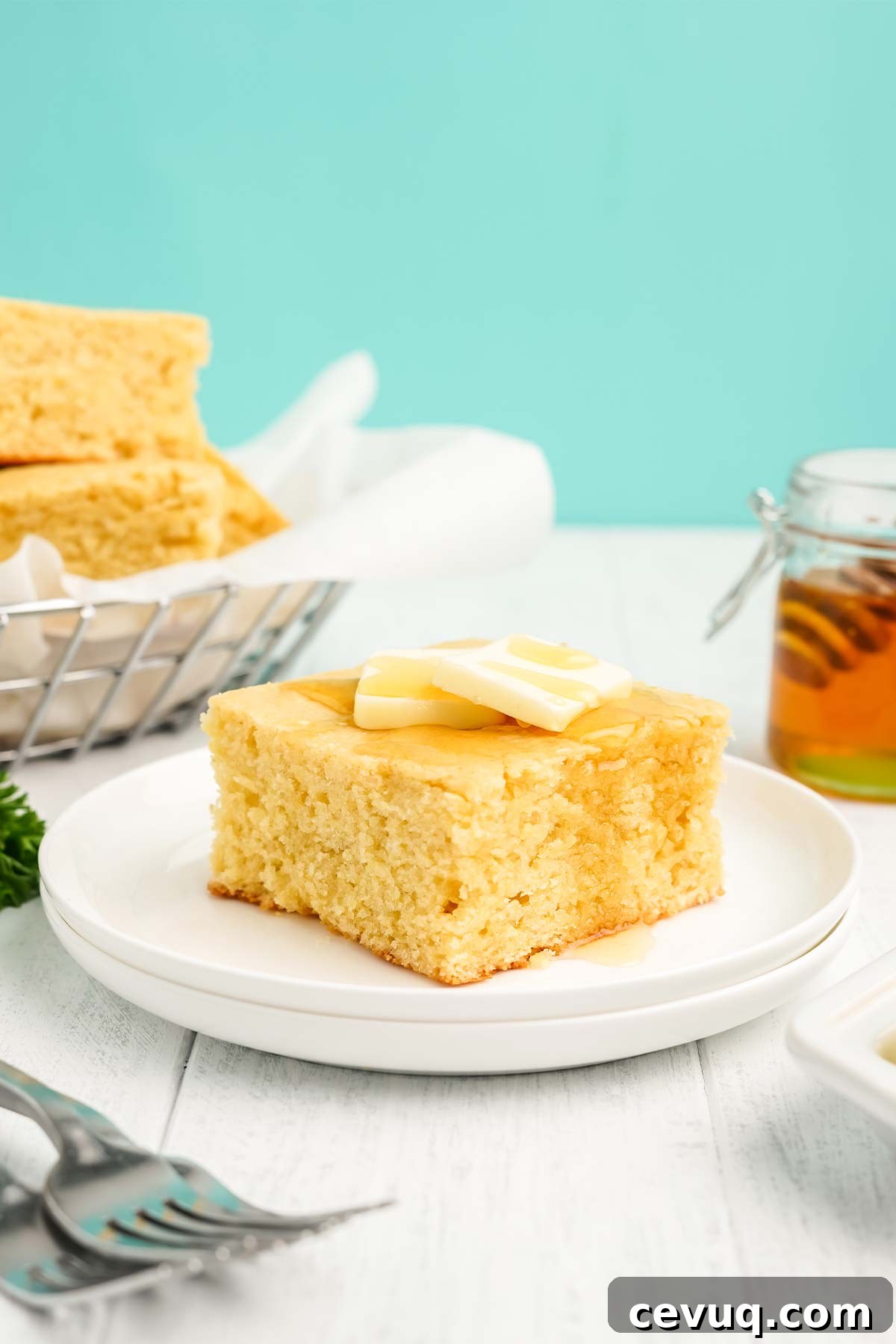 Square of cornbread with honey on a plate topped with pats of butter.