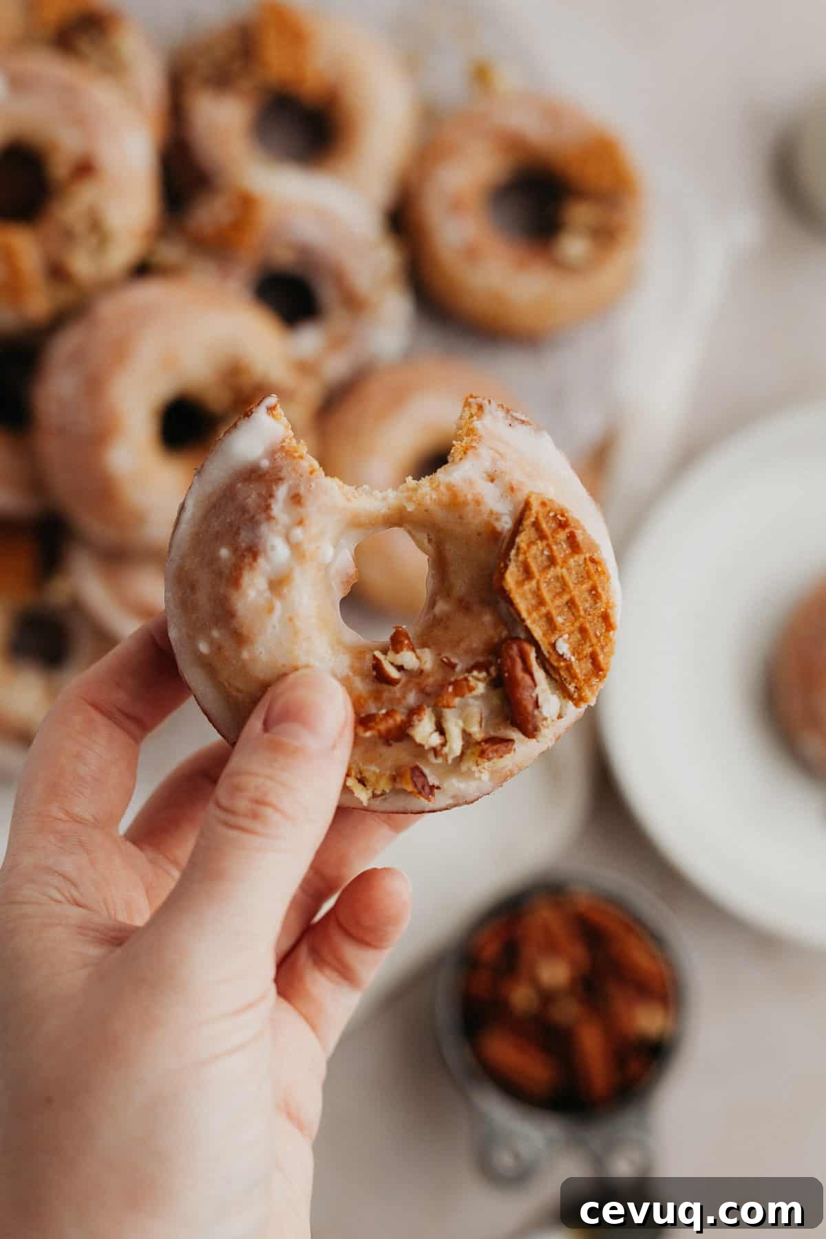 A white hand holding a doughnut that has a bite taken out of it
