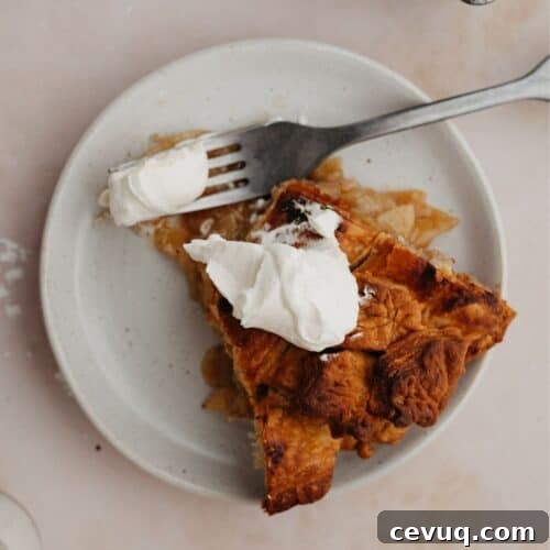 A slice of bourbon apple pie on a small plate. The pie has a dollop of whipped cream