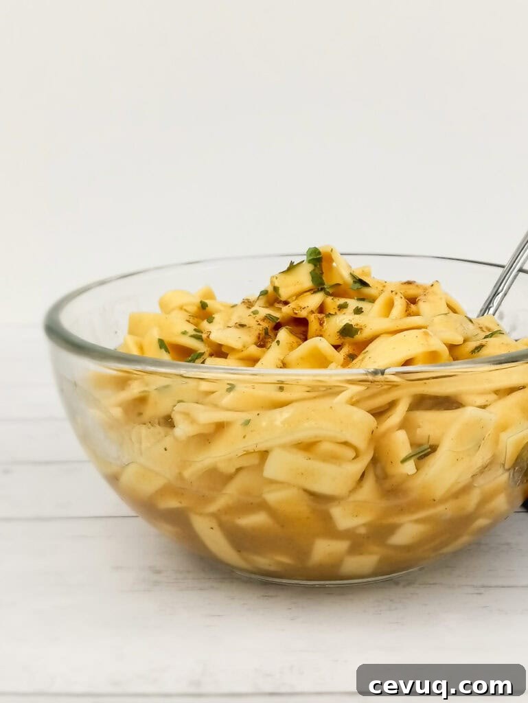 a side view of a clear bowl full of buttered egg noodles.