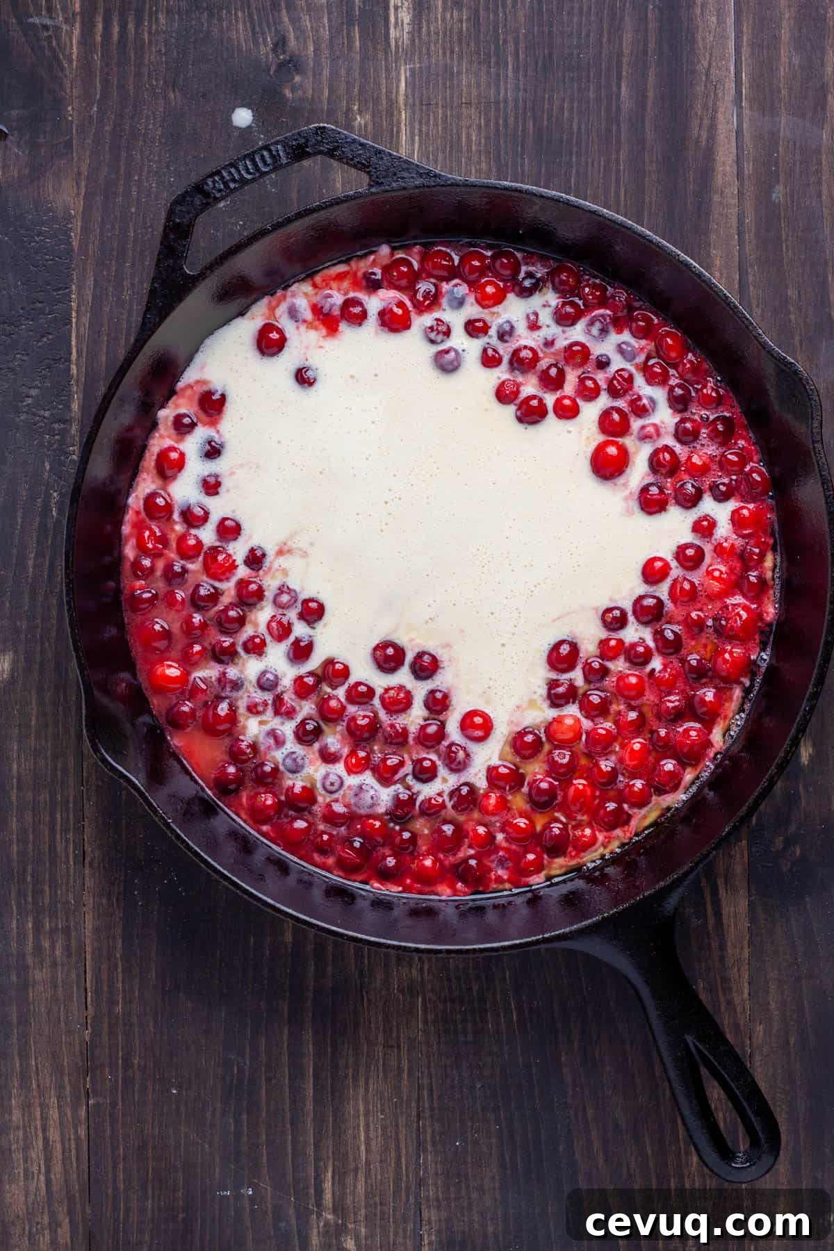 Dutch baby batter added to a large cast iron skillet with cranberries and butter in it.