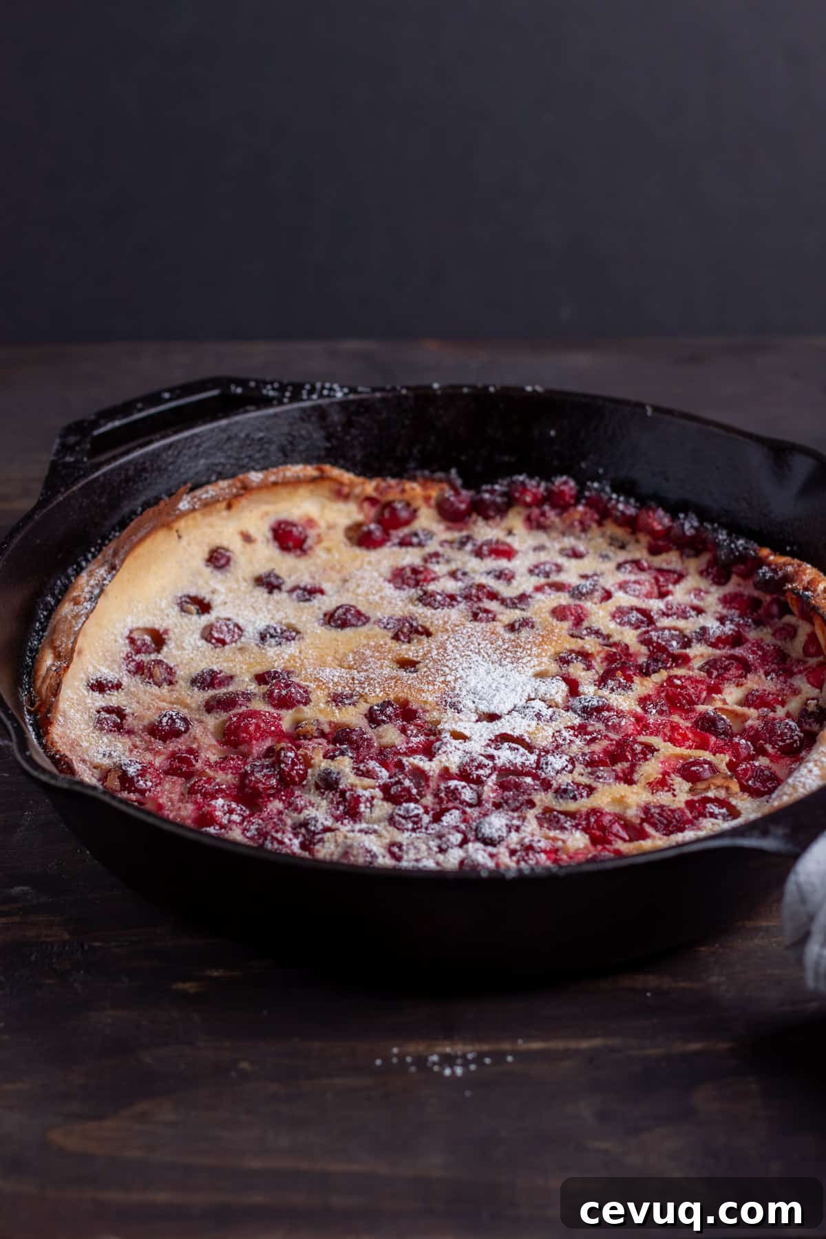 A cranberry Dutch baby in a cast iron skillet lightly dusted with powdered sugar.